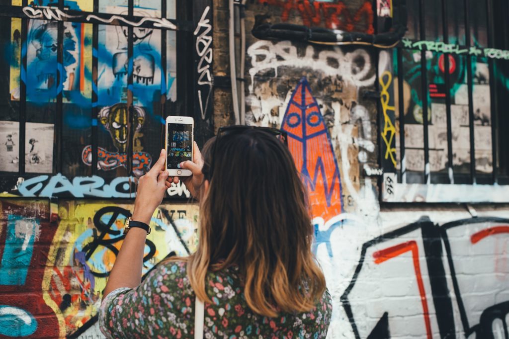 photo of a girl taking picture of a grafitii wall