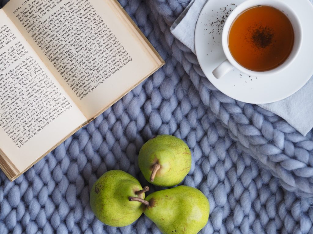 picture of tea, fruit and book on a blanket